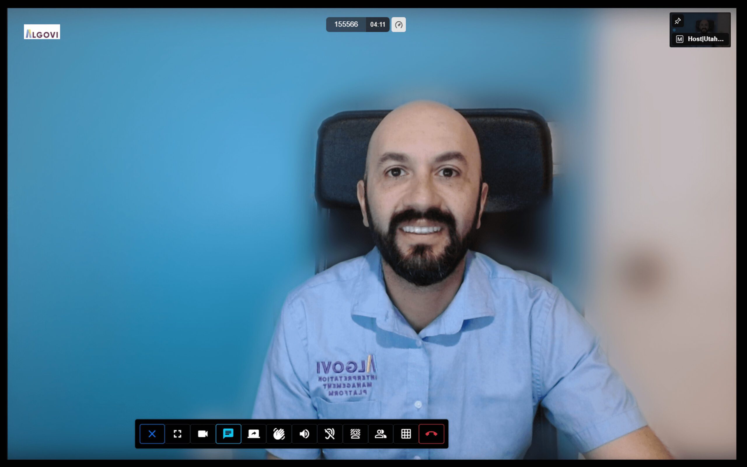 A smiling man with a beard in a collared shirt participating in a video call, seen on a computer screen with interface icons at the bottom.